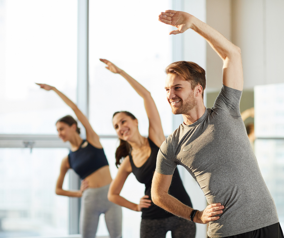 Group of adults in a fitness class stretching with one arm overhead.